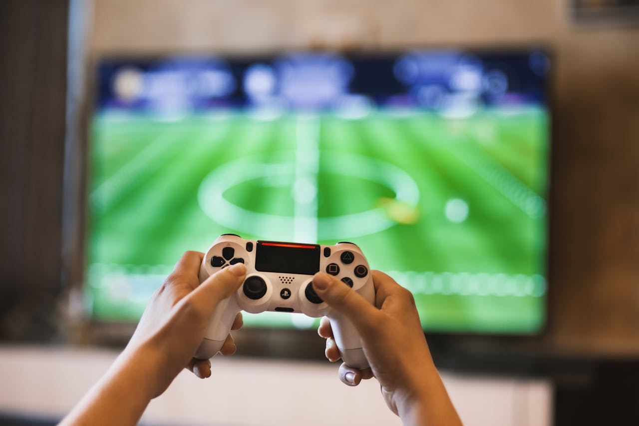 Close-up of hands holding a game controller playing a football video game on screen.